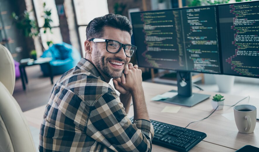 Lächelnder Programmierer arbeitet am Computer mit Code auf mehreren Monitoren.